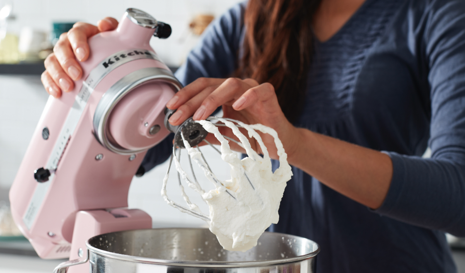 Woman holding a pink KitchenAid brand stand mixer with frosting on whisk Woman holding a pink KitchenAid brand stand mixer with frosting on whisk