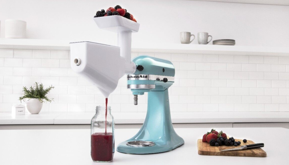 Blue KitchenAid brand stand mixer with berries inside juicing attachment and a cutting board with berries on the countertop Blue KitchenAid brand stand mixer with berries inside juicing attachment and a cutting board with berries on the countertop