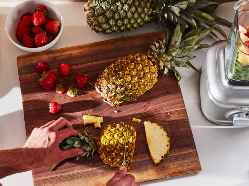 Person cutting pineapple next to a KitchenAid® blender Person cutting pineapple next to a KitchenAid® blender
