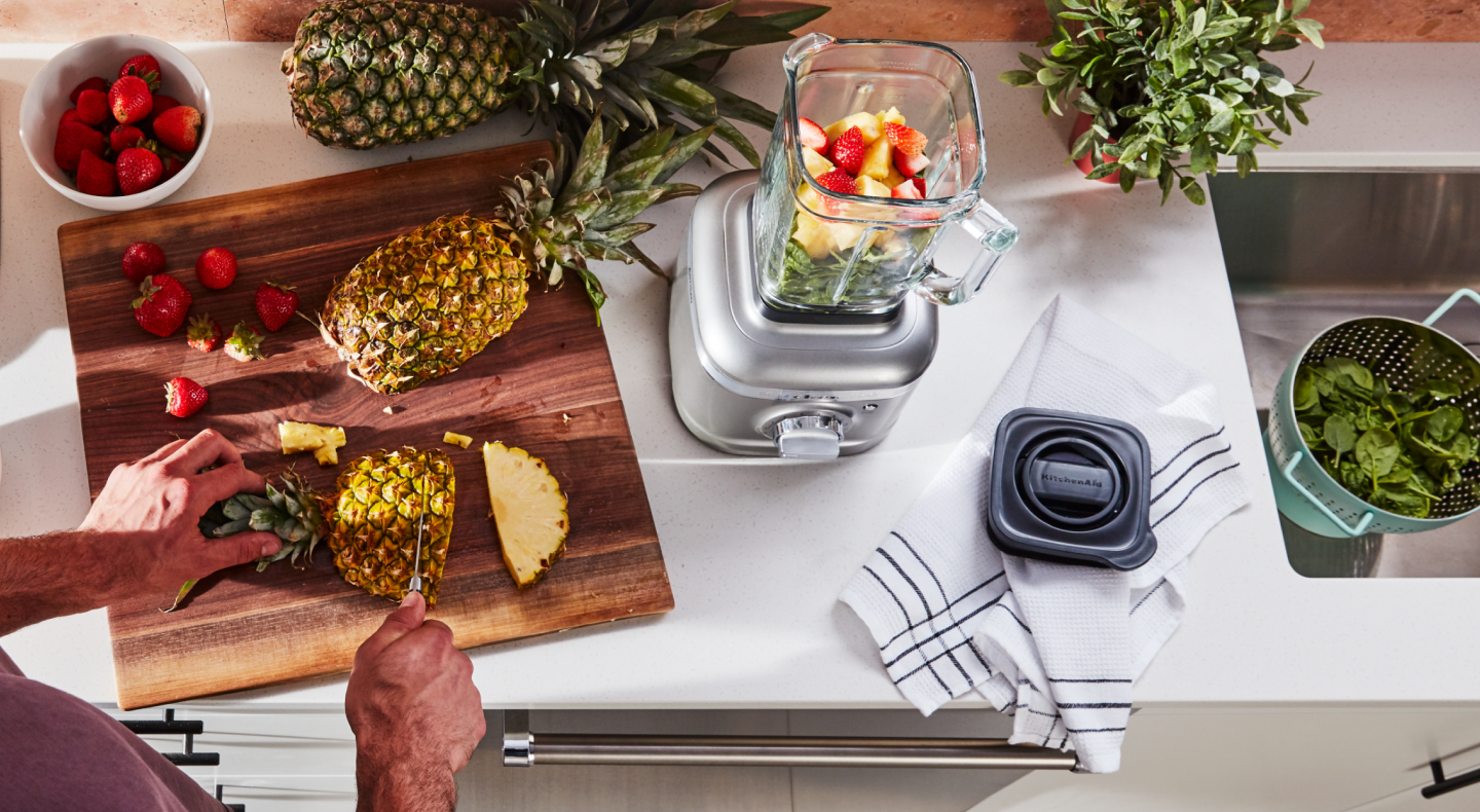 Person cutting pineapple next to a KitchenAid® blender Person cutting pineapple next to a KitchenAid® blender