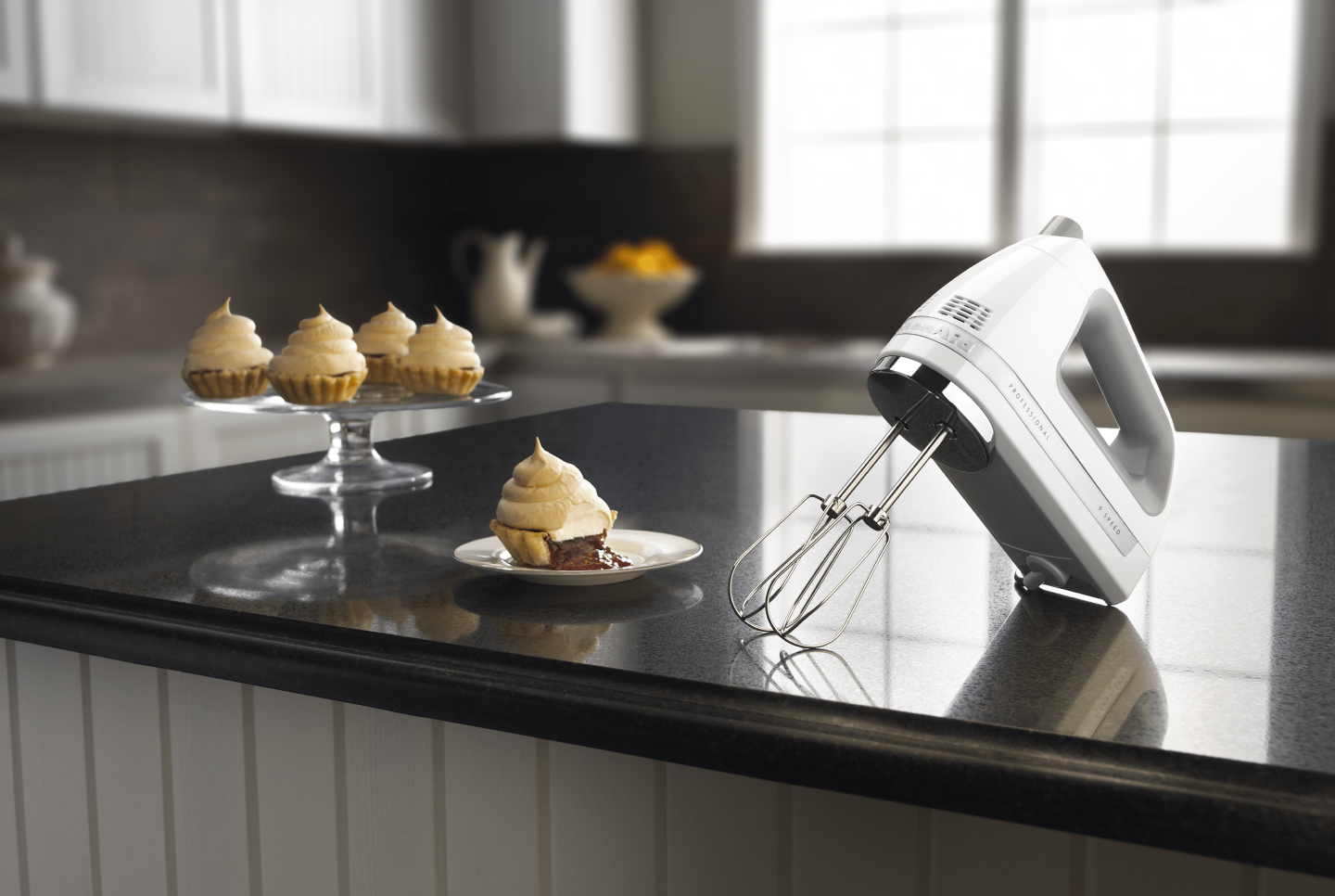 Stainless steel KitchenAid® hand mixer on countertop with cream-topped mini pie desserts Stainless steel KitchenAid® hand mixer on countertop with cream-topped mini pie desserts