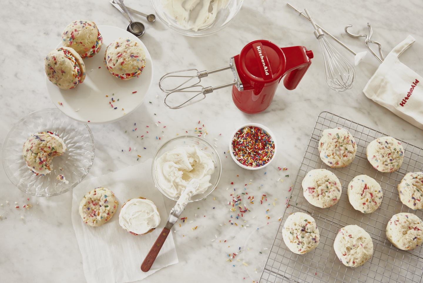 Red KitchenAid® hand mixer next to bowl of sprinkles, icing and bath of homemade cookie cream pies Red KitchenAid® hand mixer next to bowl of sprinkles, icing and bath of homemade cookie cream pies