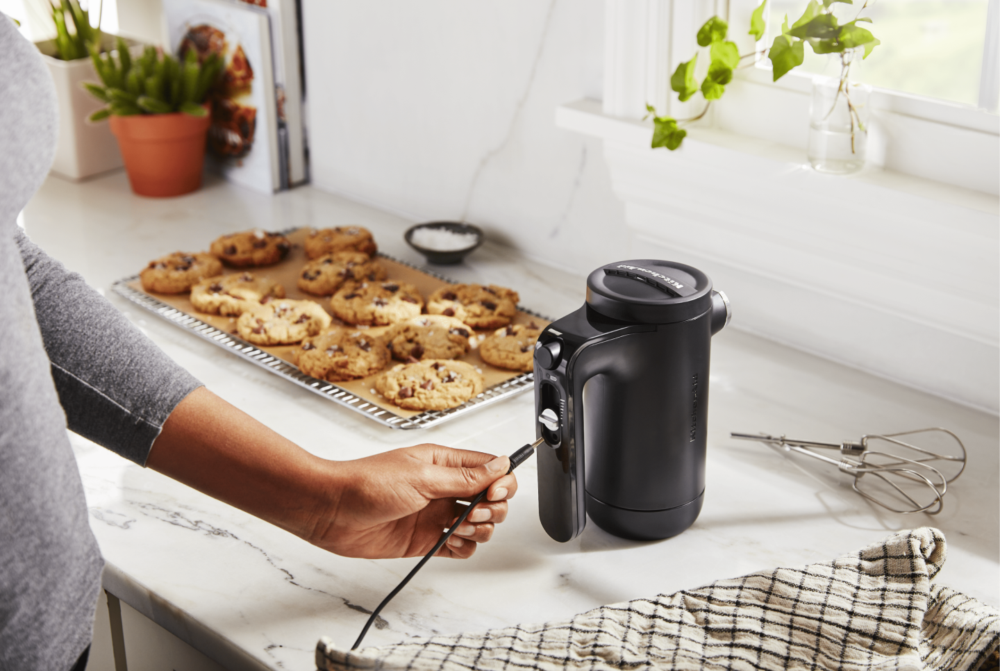 Maker plugging cord into black KitchenAid® hand mixer on countertop next to tray of chocolate chip cookies Maker plugging cord into black KitchenAid® hand mixer on countertop next to tray of chocolate chip cookies