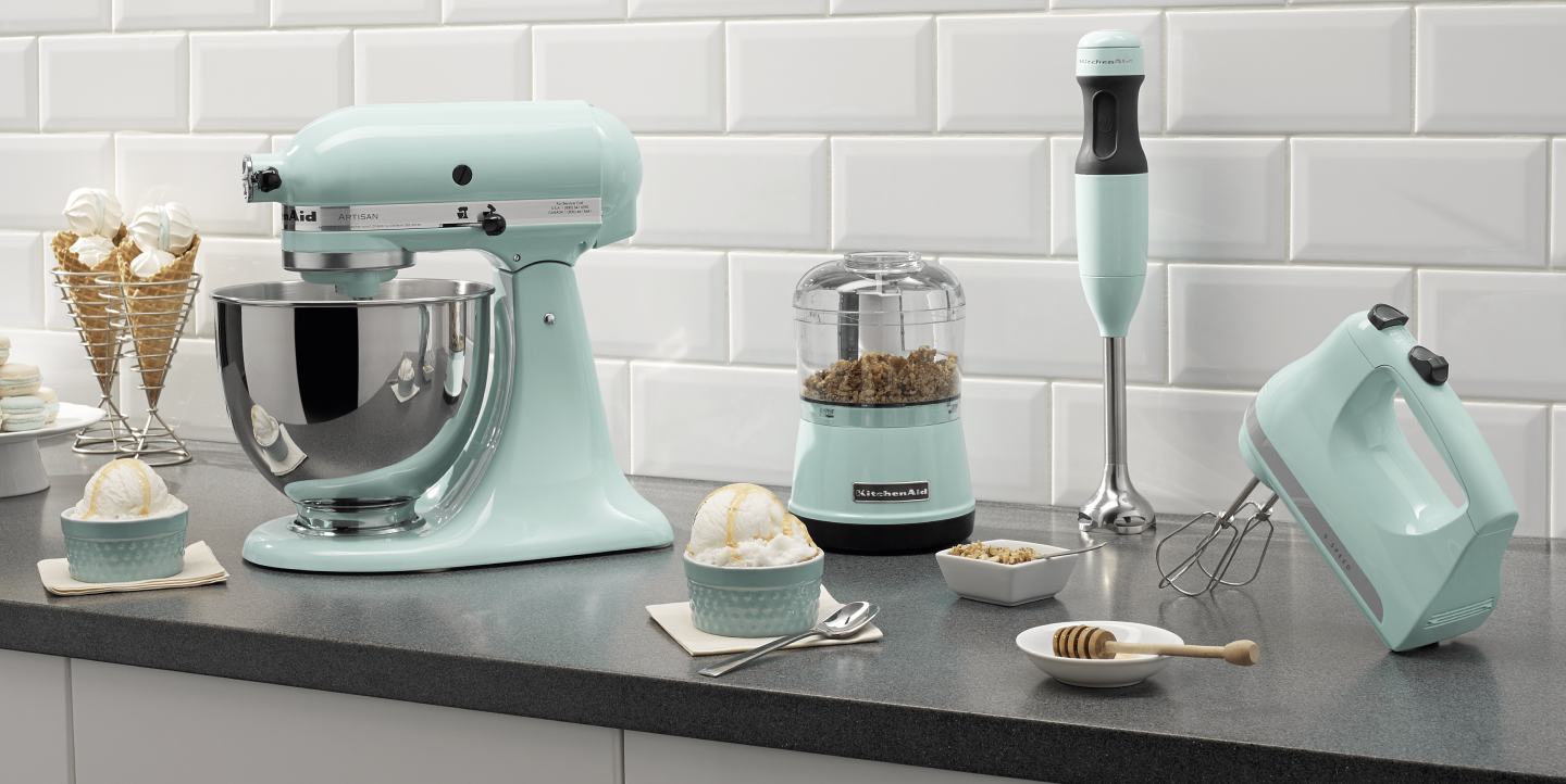 Mint green KitchenAid® food processor, stand mixer, hand mixer and immersion blender on countertop with ingredients  Mint green KitchenAid® food processor, stand mixer, hand mixer and immersion blender on countertop with ingredients