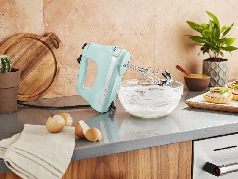 Light pistachio green KitchenAid® hand mixer on countertop with egg shells and bowl of whisked egg whites Light pistachio green KitchenAid® hand mixer on countertop with egg shells and bowl of whisked egg whites