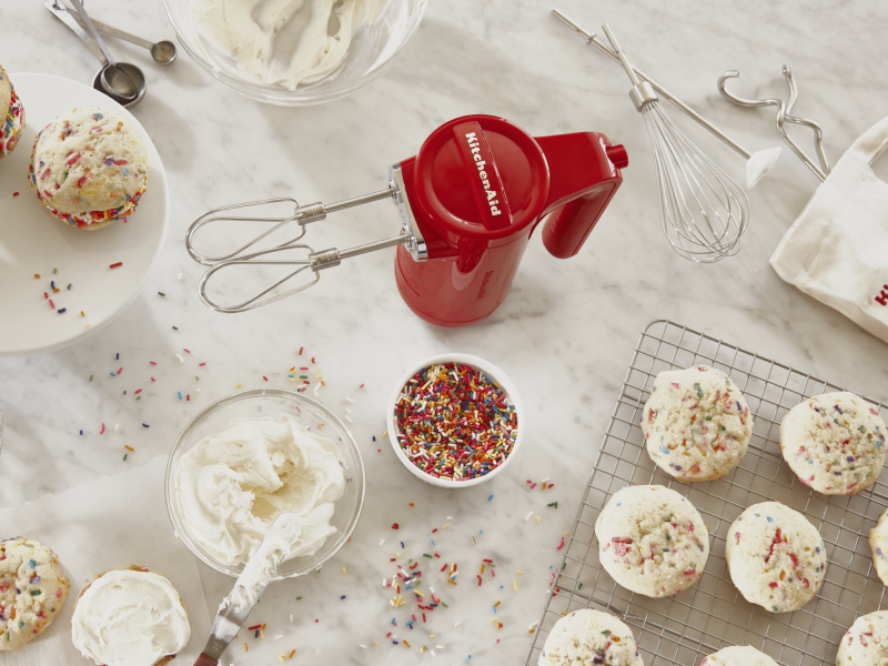 Red KitchenAid® hand mixer next to bowl of sprinkles, icing and bath of homemade cookie cream pies Red KitchenAid® hand mixer next to bowl of sprinkles, icing and bath of homemade cookie cream pies