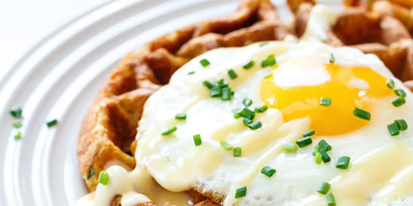 A waffle sitting on a plate, topped with a fried egg and chives. A waffle sitting on a plate, topped with a fried egg and chives.