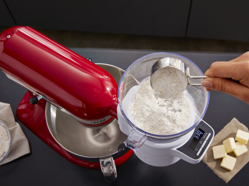 A person sifting flour into a red KitchenAid® stand mixer. A person sifting flour into a red KitchenAid® stand mixer.