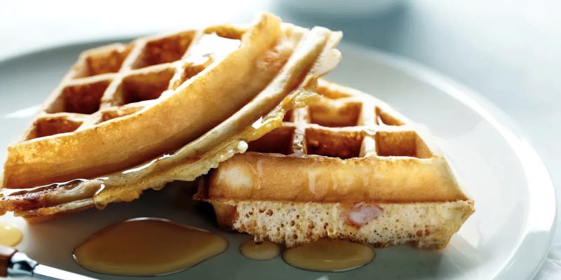 Two quarters of waffles sitting on a plate, drizzled with syrup.  Two quarters of waffles sitting on a plate, drizzled with syrup.