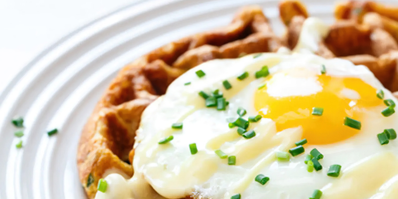 A waffle sitting on a plate, topped with a fried egg and chives. A waffle sitting on a plate, topped with a fried egg and chives.