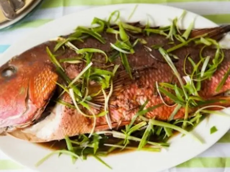Roasted whole fish on white platter with fresh herbs