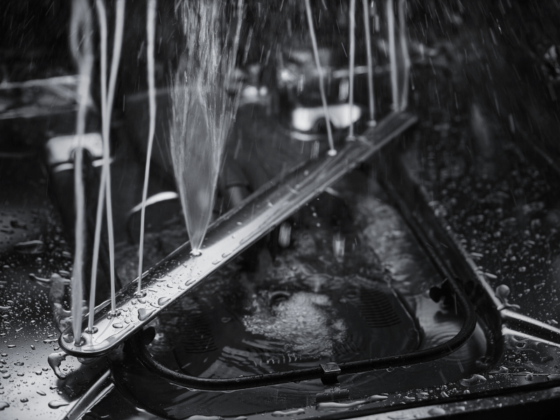 A closeup of a spray arm at the base of a KitchenAid® dishwasher spraying water.