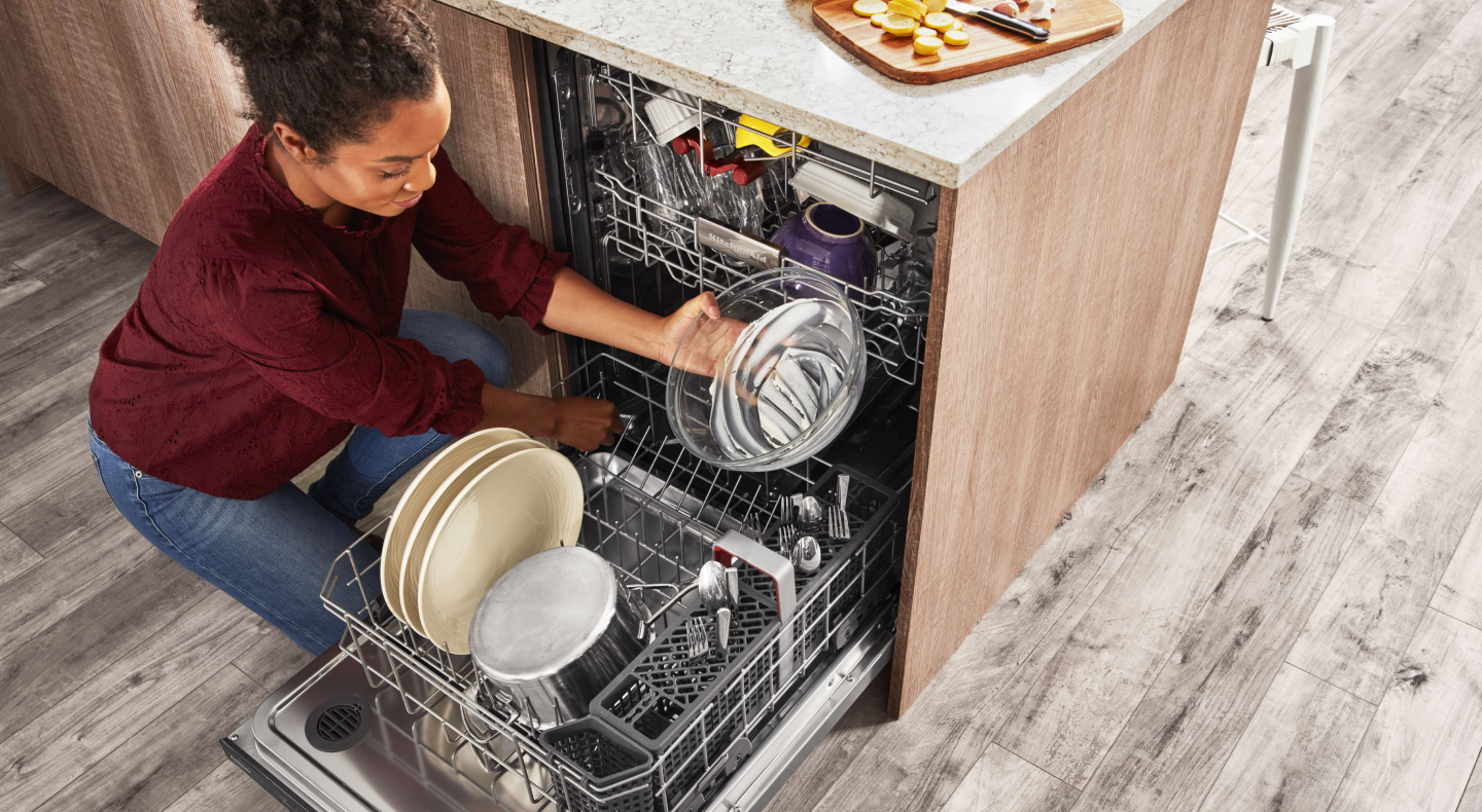 A person removing clean dishes from the bottom rack of a KitchenAid® dishwasher. A person removing clean dishes from the bottom rack of a KitchenAid® dishwasher.