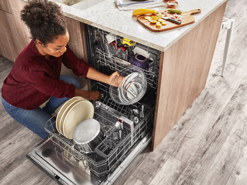 A person removing clean dishes from the bottom rack of a KitchenAid® dishwasher.