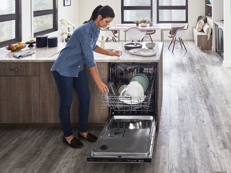 A person placing a glass on the top rack of a KitchenAid® dishwasher in a modern kitchen. A person placing a glass on the top rack of a KitchenAid® dishwasher in a modern kitchen.