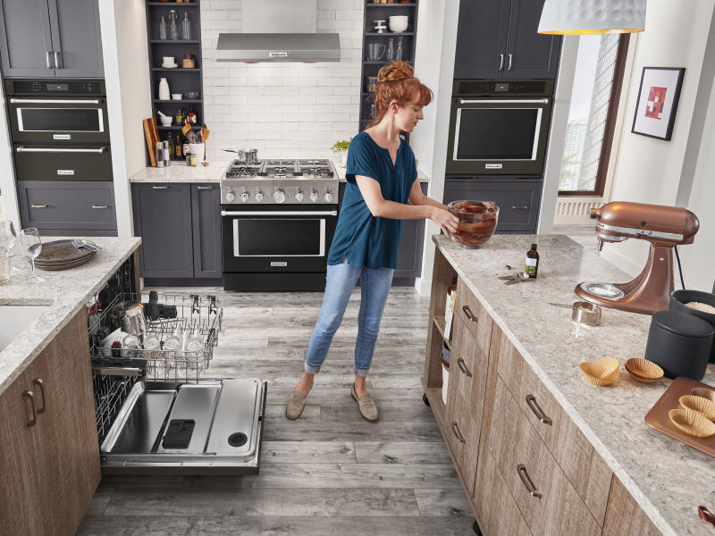 A woman placing a bowl on the counter of a modern kitchen next to a KitchenAid® dishwasher. A woman placing a bowl on the counter of a modern kitchen next to a KitchenAid® dishwasher.