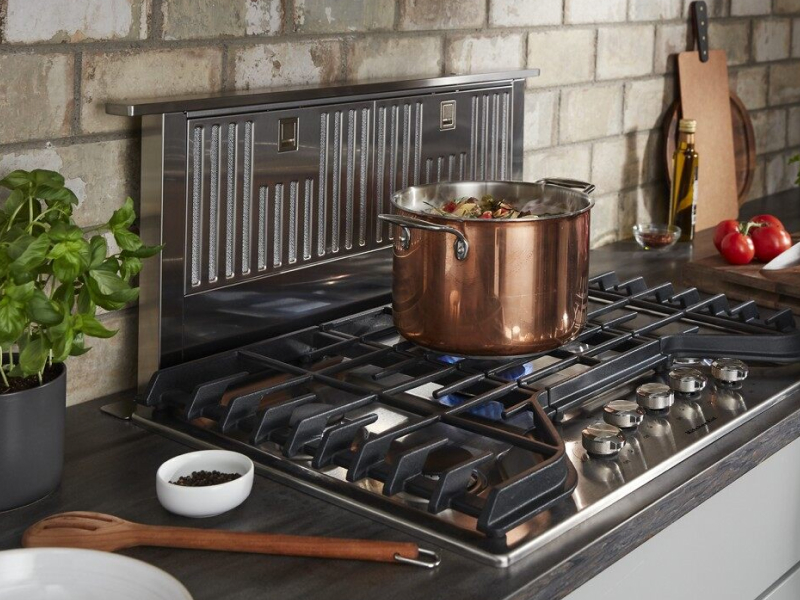 Stock pot on lit gas burner in front of a downdraft range hood
