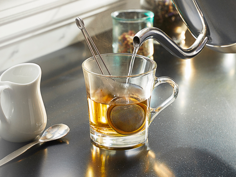 Gooseneck kettle pouring water into a glass mug to steep tea