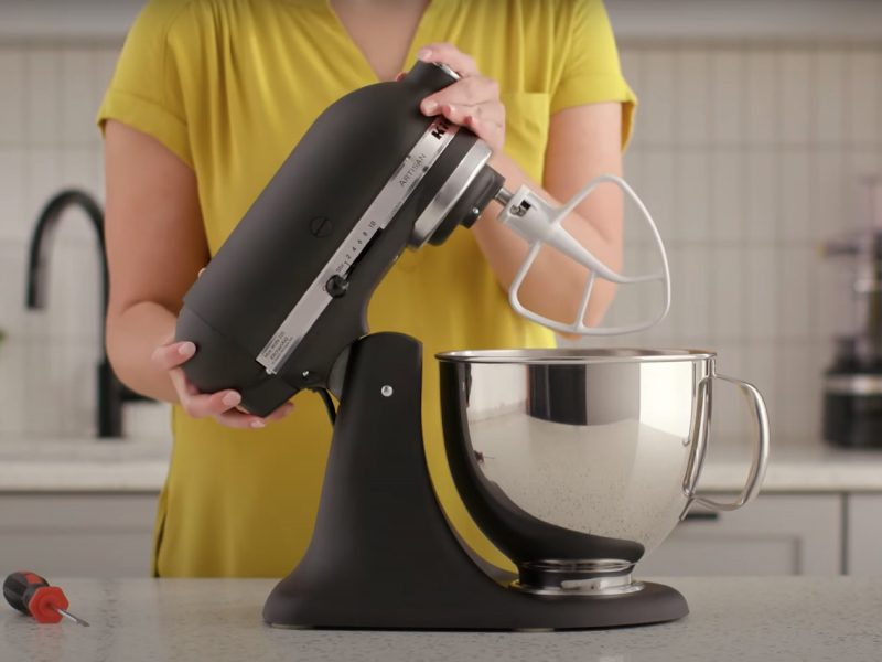 A person tilting back a black tilt-head stand mixer