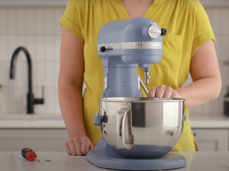 A person lowering the bowl of a blue bowl-lift stand mixer