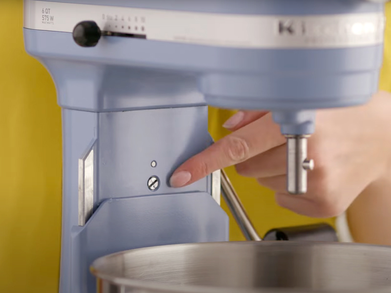 A person pointing to the screw on a blue bowl-lift stand mixer