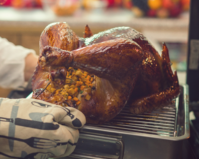Oven mitt hands pulling a roasted turkey out of the oven