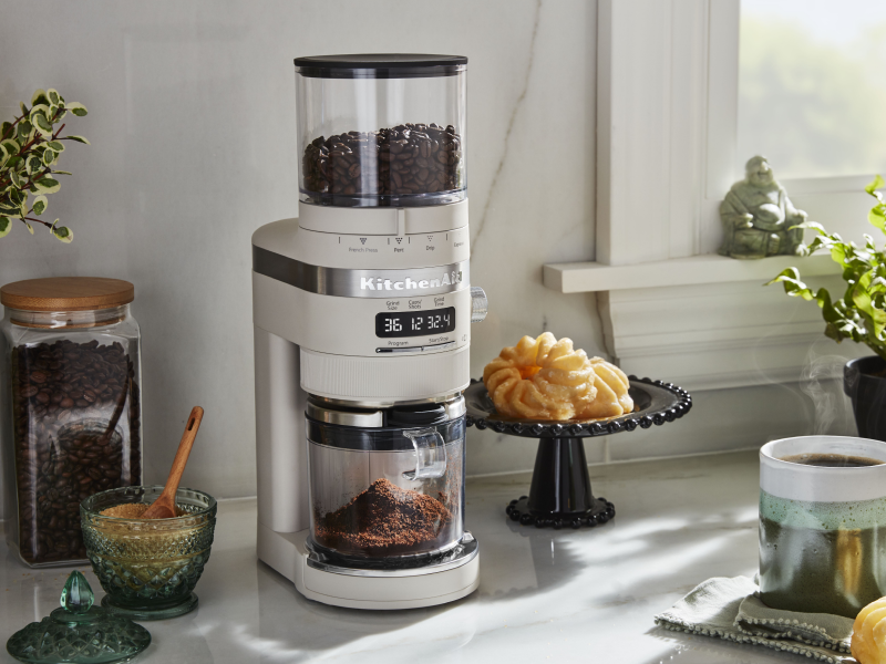 A KitchenAid® burr coffee grinder in a modern kitchen next to a pastry and cup of coffee. A KitchenAid® burr coffee grinder in a modern kitchen next to a pastry and cup of coffee.