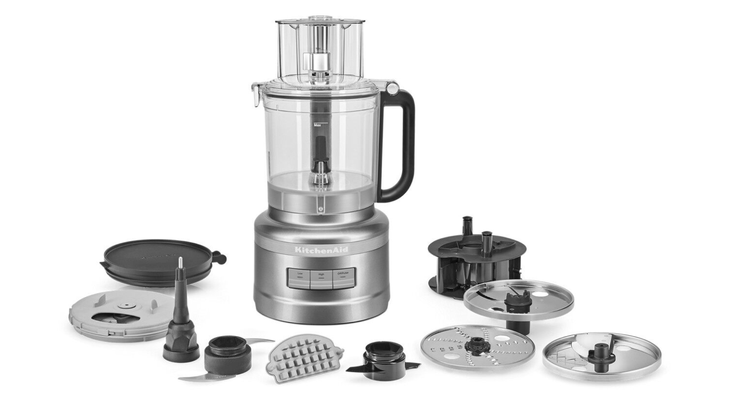 A food processor with its attachments displayed in front it. A food processor with its attachments displayed in front it.