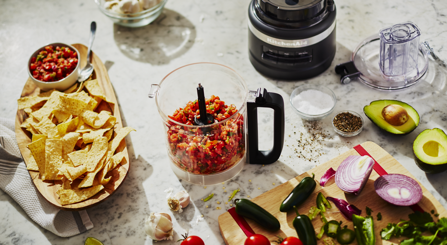 A food processor filled with salsa surrounded by the ingredients used in its creation. A food processor filled with salsa surrounded by the ingredients used in its creation.