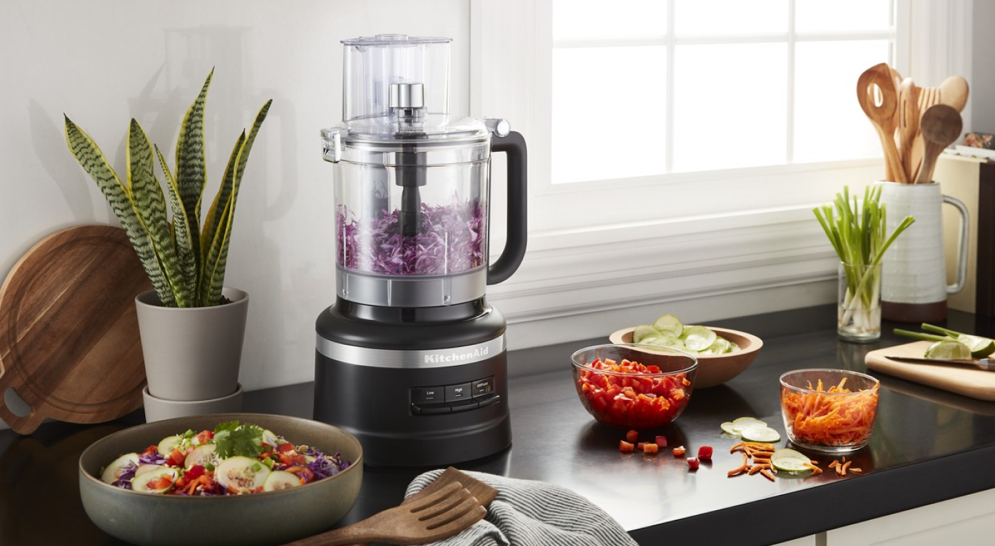 A black table that holds a food processor chopping onions as well as a fresh salad. A black table that holds a food processor chopping onions as well as a fresh salad.
