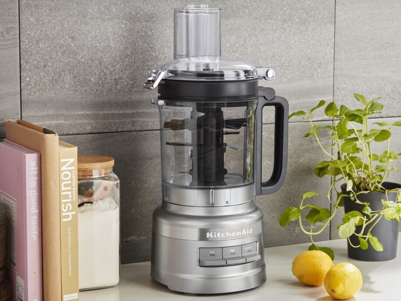 A KitchenAid® food processor sitting on a countertop next to various kitchen items