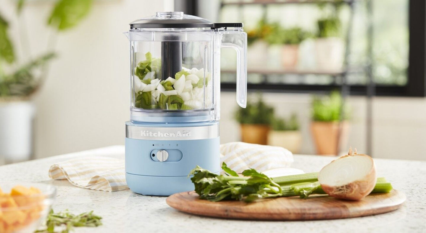 A blue KitchenAid® food processor used to cut fresh green onions