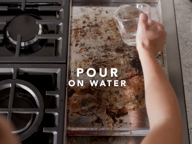 Person pouring water on dirty griddle 