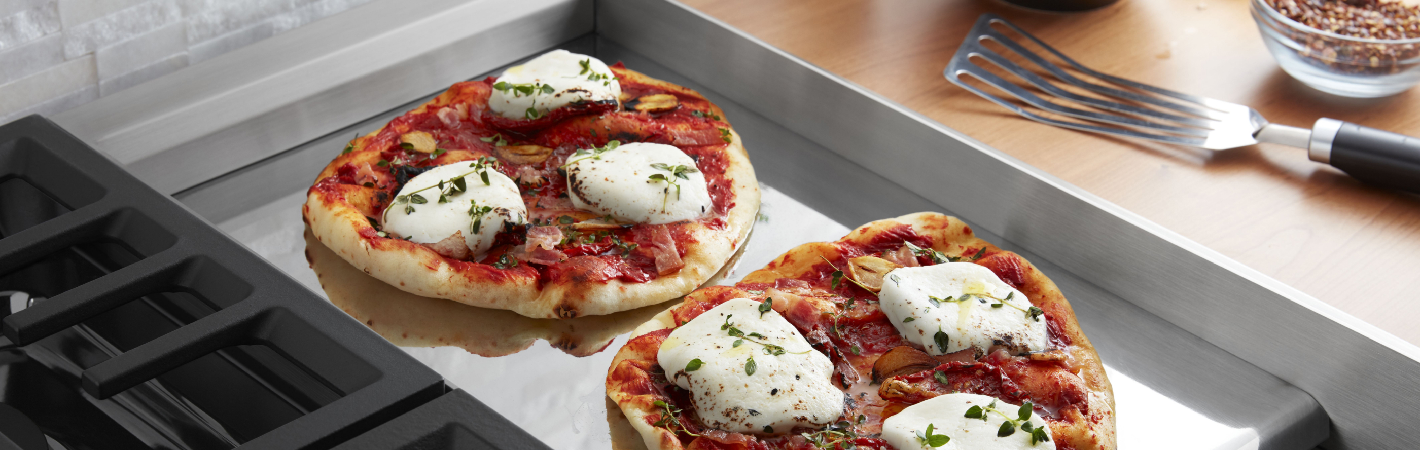 Two homemade Neapolitan pizzas cooking on a chrome electric griddle.