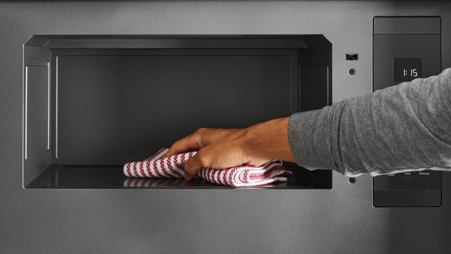 Person using a cloth to clean the interior of a microwave Person using a cloth to clean the interior of a microwave