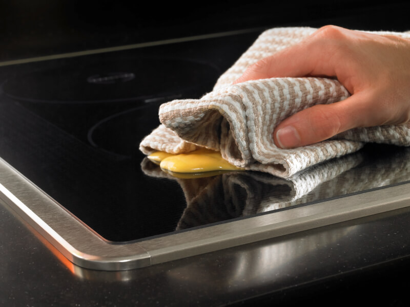 Person wiping a splatter from a stovetop Person wiping a splatter from a stovetop