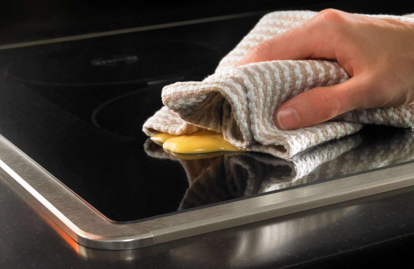 Person wiping a splatter from a stovetop Person wiping a splatter from a stovetop
