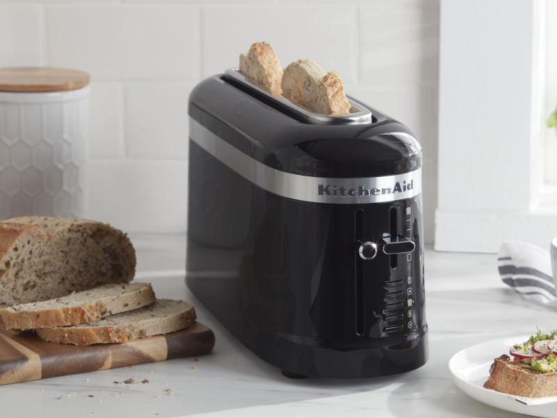 Slices of bread in a black KitchenAid® toaster next to a loaf of artisan bread and an open-faced sandwich on a modern kitchen counter. Slices of bread in a black KitchenAid® toaster next to a loaf of artisan bread and an open-faced sandwich on a modern kitchen counter.