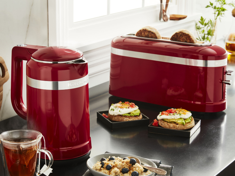 Slices of bread in a red KitchenAid® toaster next to open-faced sandwiches and cups of tea on a modern kitchen counter. Slices of bread in a red KitchenAid® toaster next to open-faced sandwiches and cups of tea on a modern kitchen counter.