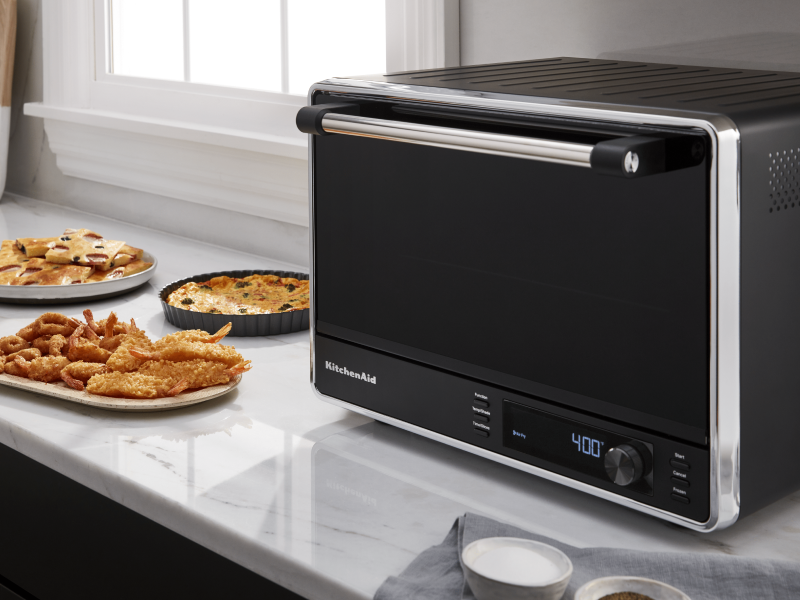 A black KitchenAid® air fryer and various appetizers on a countertop A black KitchenAid® air fryer and various appetizers on a countertop