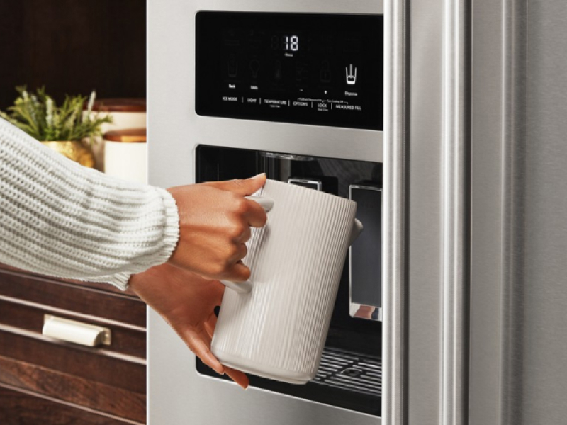 A woman filling a cup with water from a KitchenAid® refrigerator