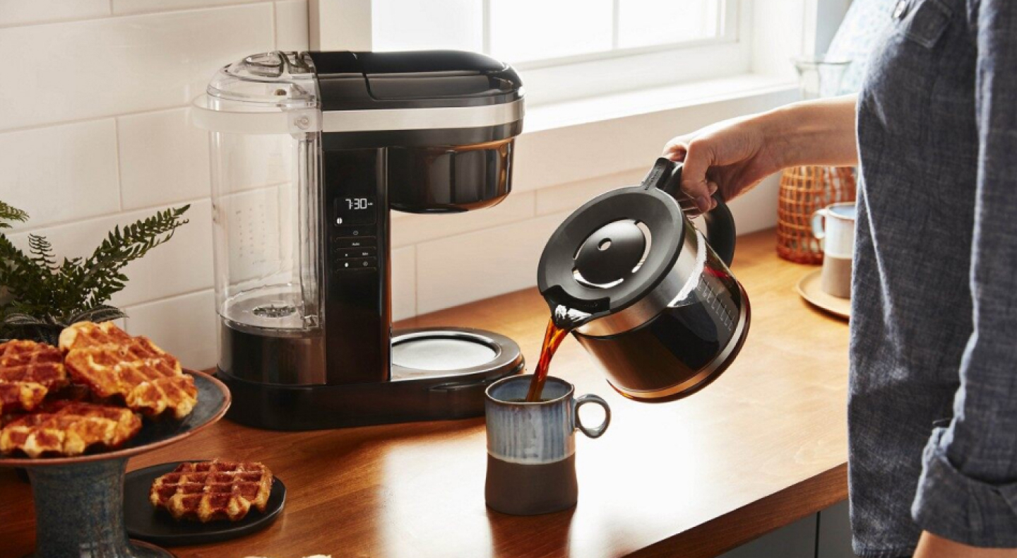 Woman pouring coffee into a mug with drip coffee maker in background Woman pouring coffee into a mug with drip coffee maker in background