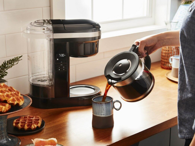 Woman pouring coffee into a mug with drip coffee maker in background Woman pouring coffee into a mug with drip coffee maker in background