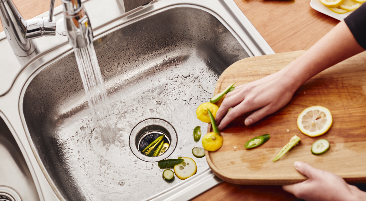 Person scraping vegetable scraps into a stainless steel sink Person scraping vegetable scraps into a stainless steel sink
