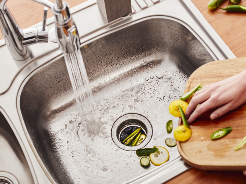 Person scraping vegetable scraps into a stainless steel sink Person scraping vegetable scraps into a stainless steel sink