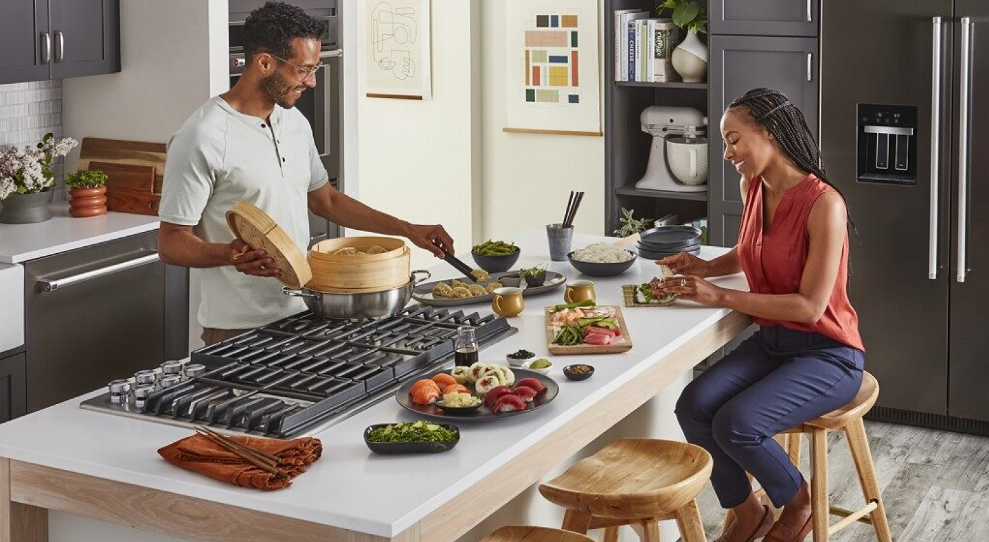 A man and woman preparing various dishes with a stovetop A man and woman preparing various dishes with a stovetop