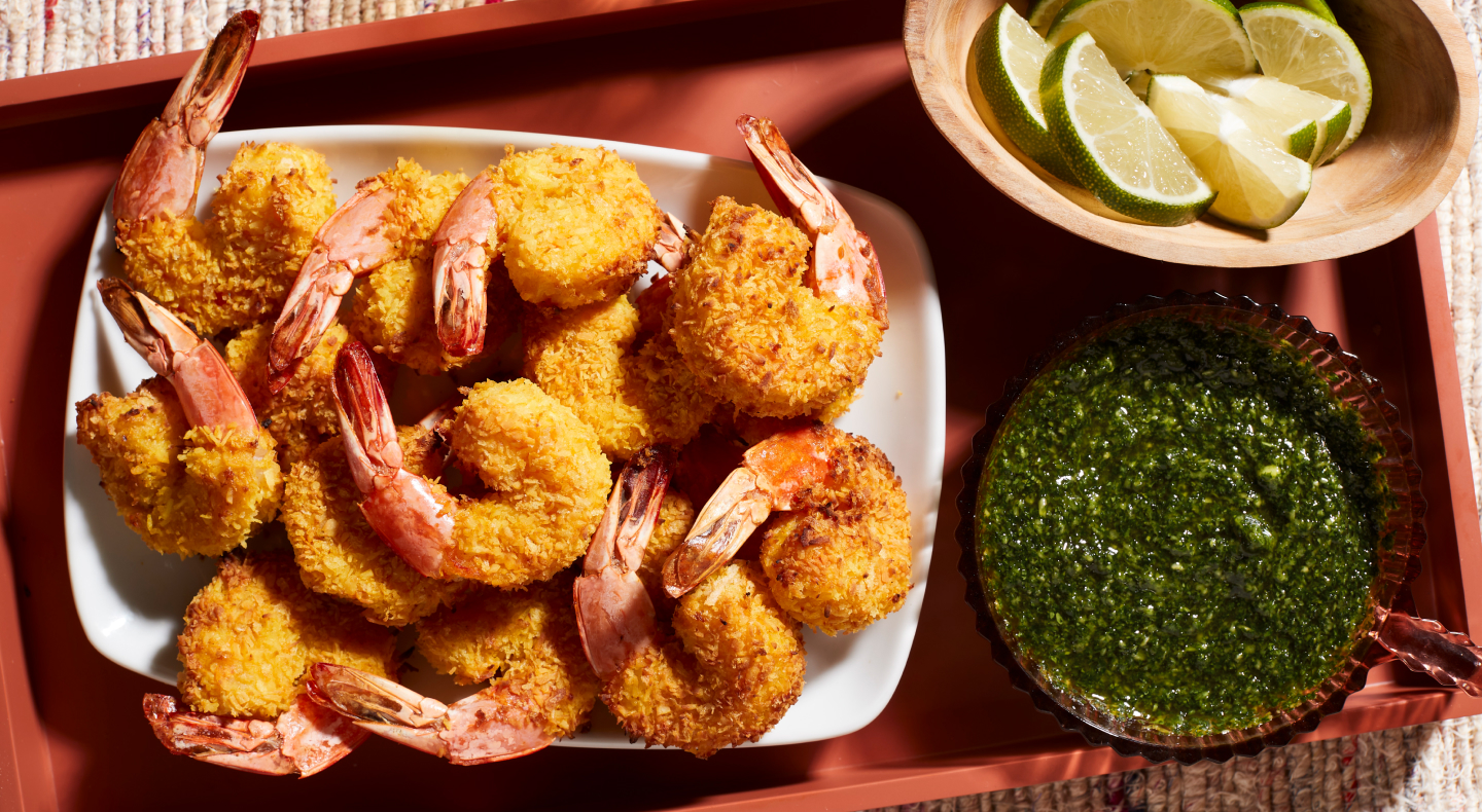 A closeup of air fryer shrimp on a serving tray next to a fresh sauce and lime slices. A closeup of air fryer shrimp on a serving tray next to a fresh sauce and lime slices.