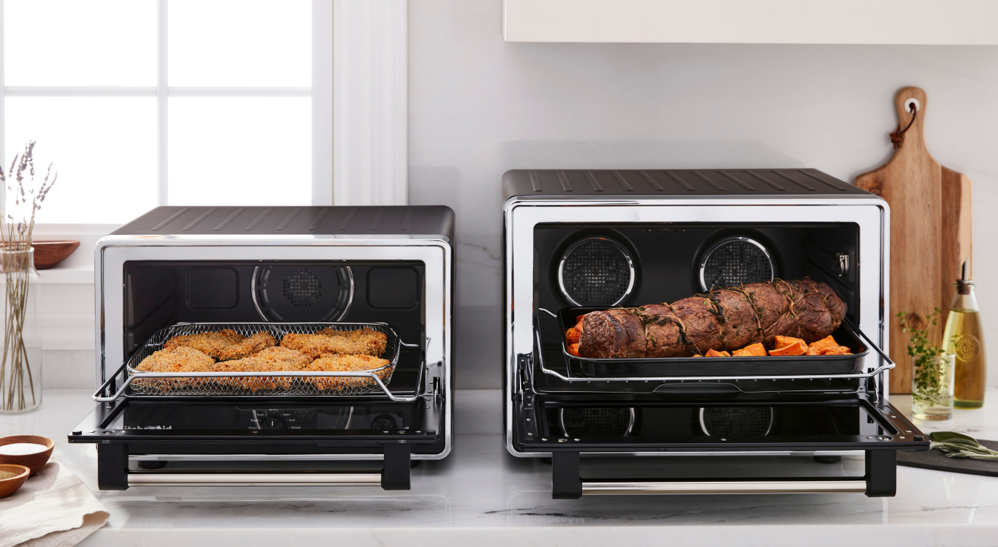 Two KitchenAid® countertop ovens with freshly prepared food on a modern kitchen counter. Two KitchenAid® countertop ovens with freshly prepared food on a modern kitchen counter.