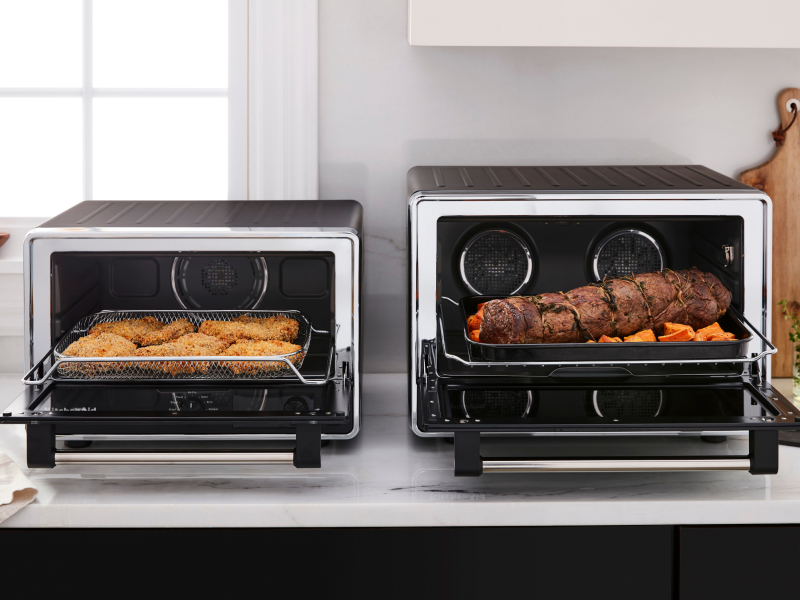 Two KitchenAid® countertop ovens with freshly prepared food on a modern kitchen counter. Two KitchenAid® countertop ovens with freshly prepared food on a modern kitchen counter.