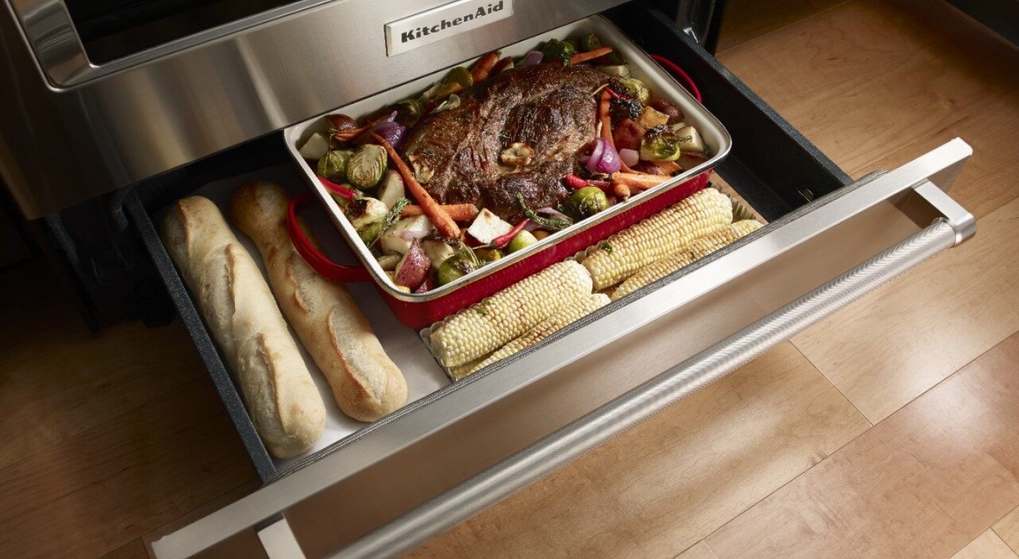 Open warming drawer with bread, a roast and vegetables inside Open warming drawer with bread, a roast and vegetables inside